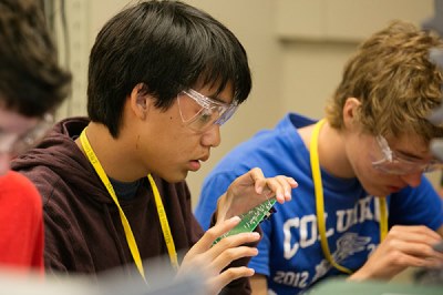 A student stares at a circuitboard while wearing safety goggles