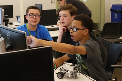 Students point excitedly at their computer screen while programming a small robot
